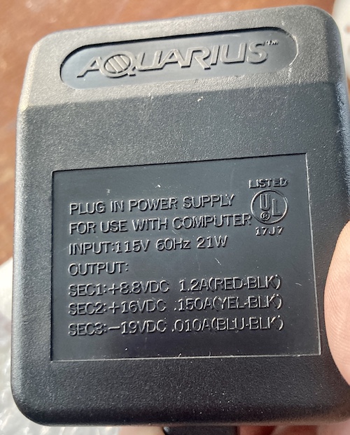 The label on a Mattel Aquarius power supply unit. It says "plug in power supply for use with computer." Input 115V 60Hz 21W, Output: SEC1 +8.8VDC 1.2A (red-black), SEC2 +16VDC 0.150A (yellow-black), SEC3 -19VDC 0.010A (blue-black.)