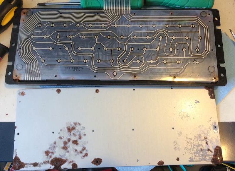 The backing plate of the keyboard is off. It's extremely rusty, with the paint flaking off in big chunks. The membrane is exposed.