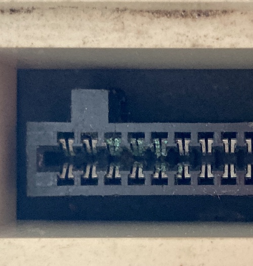 Green corrosion blooming on eight of the pins of the cartridge slot. The plastic surrounding it has a lot of loose black dirt.
