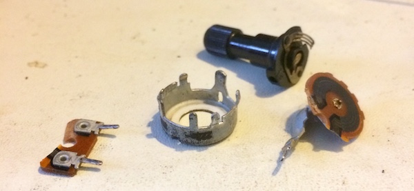 The dismantled potentiometer. There are three major parts: the metal housing, the sprung-wiper knob, and the PCB substrate.