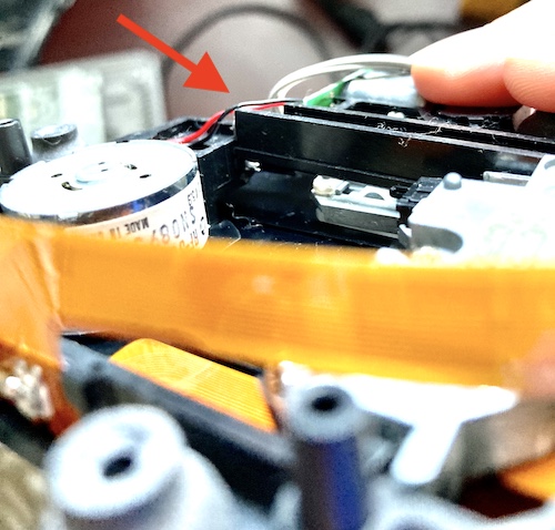 I am holding the disc-drive assembly upside down. There is a red arrow pointing to the piece of plastic that is jutting out at an awkward angle.