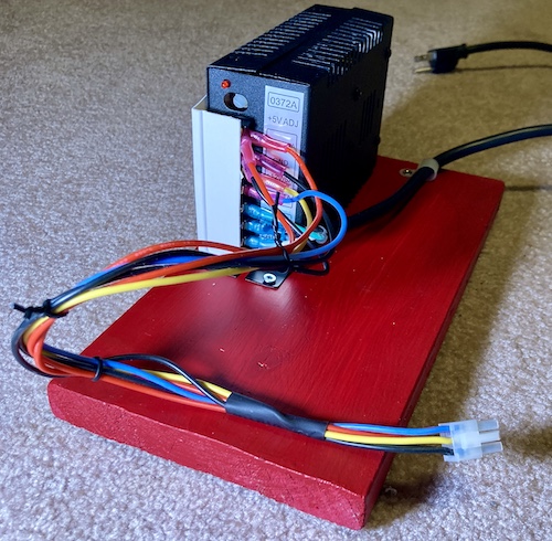 The power supply is screwed down to a piece of red 2x4. The wiring harness is held together with old twist-ties, and the whole thing looks even worse than before, if that's possible.