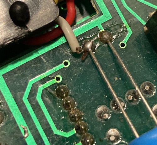 A wire is insufficiently tinned and badly soldered to the unclipped legs of a cap. There's flux everywhere, and stray solder blobs. The solder mask is deteriorating.