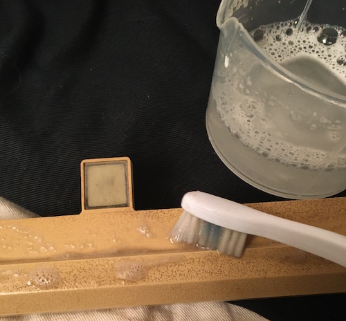 A toothbrush with the Oxy-Clean mixture is wiping clean the keyboard plastic. On the right, filth. On the left, clean plastic.