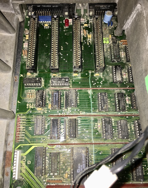 Water and biohazard damage to the logic board, as seen from the card cage with the top removed. Many ICs have green-blue legs, indicating copper corrosion.