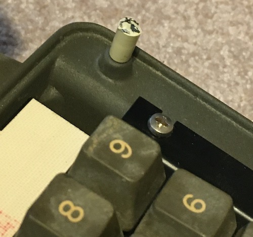 A snapped post on the plastic cover for the keyboard. It has some black adhesive on it, likely a kind of epoxy.