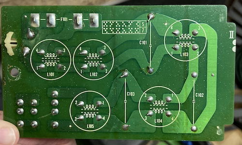 The underside of the power entry board. Solder joints for fuses can be seen, as well as an explanation of the strange round objects as being some kind of choke around a wire.