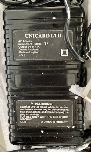 The label of the AC adapter. It says UNICARD LTD - input 240V - 50Hz, output 9V at 1A. Double insulated. Made in England.