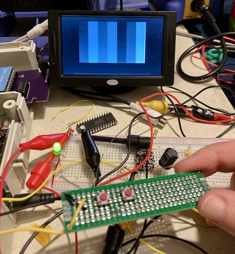 The backup camera LCD is now displaying a monochrome colour bars pattern. In the foreground is a sketchy protoboard with two buttons, and in the background is the sketchy solderless breadboard containing the composite mod under development. The logic probe, not shown, is also connected to power and ground using alligator clips. Between the backup camera monitor and the breadboard, you can see a 27sf256 that I broke the Vcc pin off of when I was trying to remove it from the PCB. I have ham for hands.