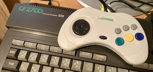 A white game controller, reading "FM2AND6," is sitting on top of the stark black National CF2700 MSX.
