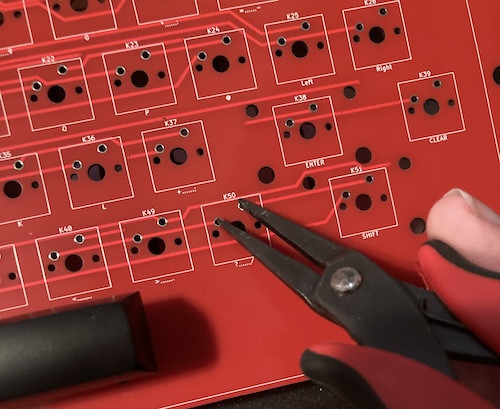 I am touching the pins of the question-mark key switch's footprint with a pair of pliers.