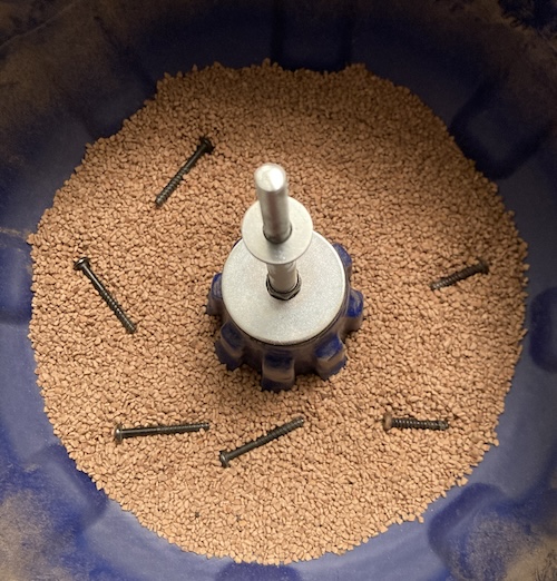 The screws are thrown into a blue vibratory tumbler bowl.