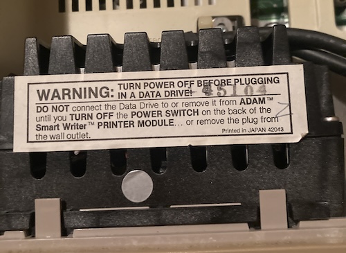 The sticker on top of the tape drive reads: WARNING turn power off before plugging in a data drive! Do NOT connect the data drive to, or remove it from, ADAM until you turn off the POWER SWITCH on the back of the Smart Writer PRINTER MODULE... or remove the plug from the wall outlet. Printed in JAPAN 42043. The serial number "45104" is stamped on top.
