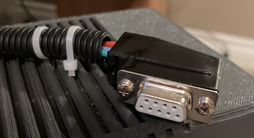 The business end of the power supply. Multi-coloured wires are stuck inside some poorly-applied cheap split-loom tubing, fastened with zipties. They go into a right-angle female DE9 connector.