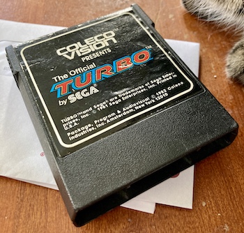 A copy of Turbo, now with an English label ("The Official Turbo by Sega") is threatened by a cat. Please don't judge how ugly my kitchen table is, I swear I am going to resurface it soon.