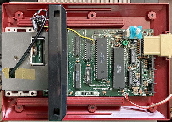 The Famicom sitting half-assembled. The motherboard is sitting loose in the red plastic base, and the mod PCB is dangling in the middle of the air.