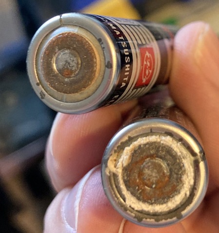 A closeup of the leaky negative side of the batteries. One is very dusty with a chalky, white coating.