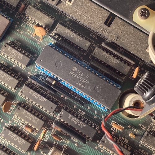 The new HD63C09EP CPU is installed into the socket. The eerie light illuminates a forest of dust that I haven't bothered to clean off the board.