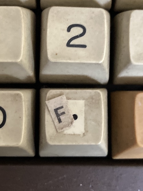 The "F" sticker is falling off of the decimal point key on the number pad. You can see that the grungy key is very, very clean behind the sticker.
