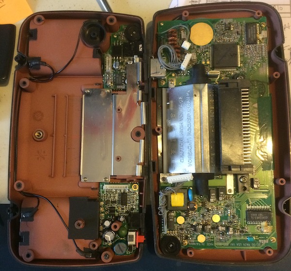 The Game Gear lays open on the desk, exposing the circuit boards in need of repair.