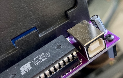 The USB-B power jack, next to a 27SF256 BIOS EEPROM that has had a leg grafted back onto it.