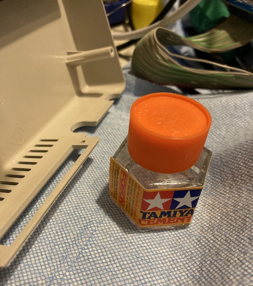 The plastic "lip" is re-aligned and sealed with a bottle of Tamiya model cement, placed nearby. The entire mess is sitting on some blue shop towel to catch any drips.
