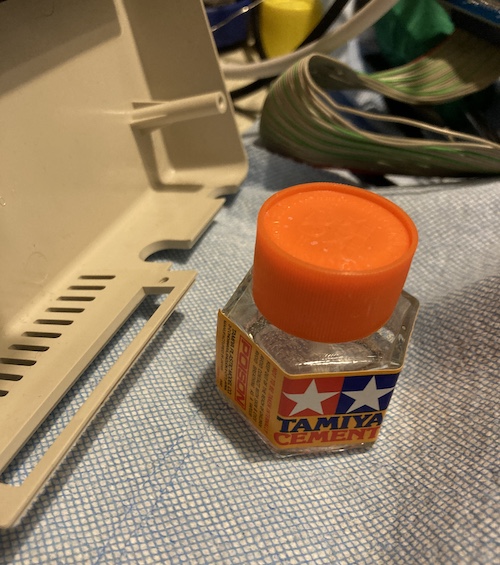 The plastic "lip" is re-aligned and sealed with a bottle of Tamiya model cement, placed nearby. The entire mess is sitting on some blue shop towel to catch any drips.