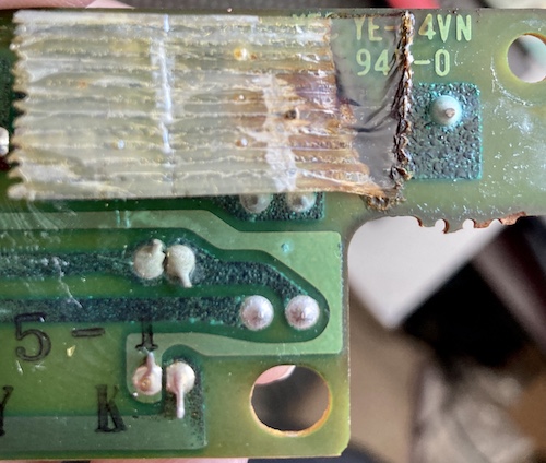 The backside of the PCB. You can see that the entire pad that used to hold the negative side of the battery is blossoming with blue-green corrosion. As well, two traces nearby are eaten up by it. There's some cellophane tape that has melted and turned black where the leakage touched it.