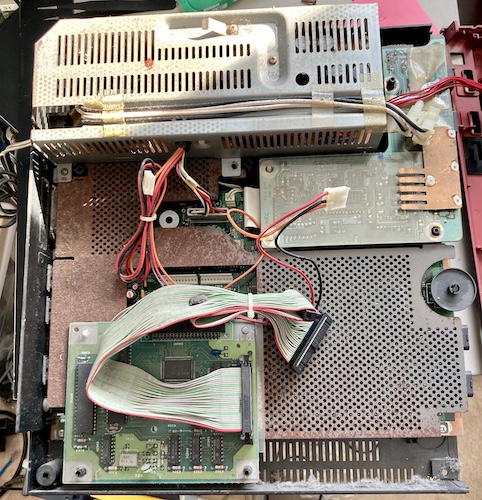 The top case is removed, showing the floppy card, power supply, loose front case and rusty metal shielding surrounding the motherboard.
