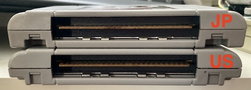 A Japanese cartridge (top) and a US cartridge (bottom) are compared. The recess for the tabs on the US cartridge are out at the extents of the case, and the Japanese cartridge are closer to the clips holding the back on.