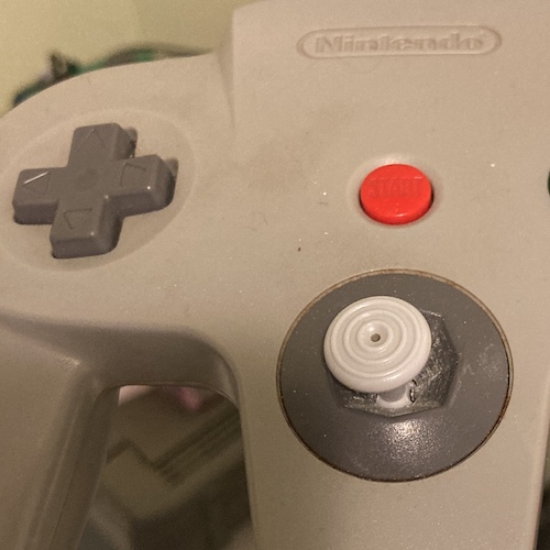 A worn control stick in a grey N64 controller. It's tilting to the left, loosely, and is surrounded by a white powdery substance in the receiver.