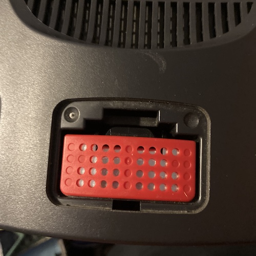 Hooray! A red Expansion Pak is loaded into the Memory Expansion slot at the front of the Nintendo 64. It has many cooling holes and a nice shiny metal body.