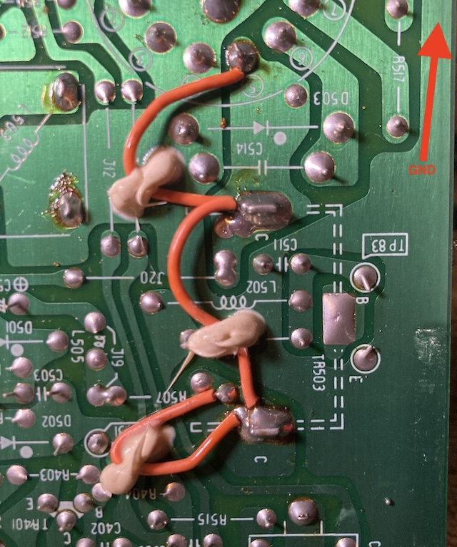 The underside of the TR503. The shield is used as the "C" for collector pin, and there are two other pins marked "B" for base and "E" for emitter. The "E" pin is connected to a large pour which goes up the edge of the board to a pin marked "GND" which is just out of shot. An ugly orange bodge wire is connected to the collector pin to multiple test points, and affixed using some nasty-looking beige glue.
