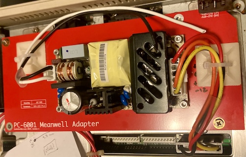 The Meanwell is now turned around, so that the output side is on the right side of the board. A white-and-black mains cable worms around the power supply on the top and is held in place by a giant self-adhesive ziptie pyramid.