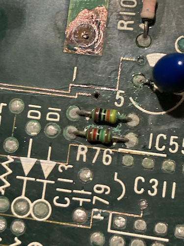 Starting to strip back the solder mask. Some traces are now exposed as bright copper, and residue from the scraping is nestling under R75 (top) and R76 (bottom). You can see that some vias nearby are blackened by significant corrosion damage. A resistor up at the top no longer has colour bands on it.