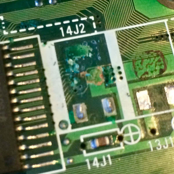 The debris left behind under the 14J2 electrolytic capacitor. There is bright green battery discharge as well as brown glue residue.