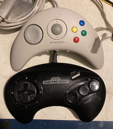 The Pippin controller (top, white) compared in size to the Genesis 3-button controller (bottom, black.) Notice how much bigger the buttons on the Genesis pad are.