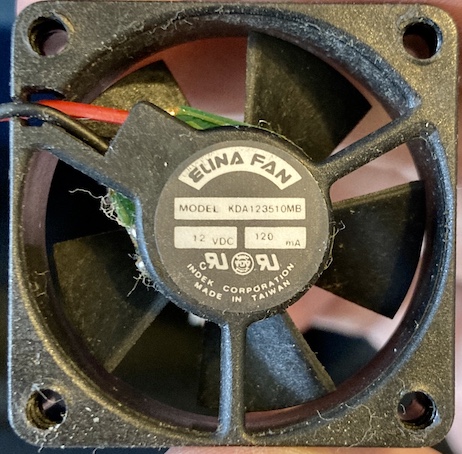 The fan has been removed from the Pippin. It is covered in gross hair and dust, and says ELINA FAN, MODEL KDA123510MB. 12 VDC, 120mA INDEK CORPORATION, MADE IN TAIWAN