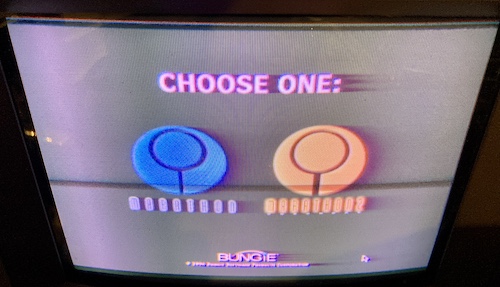 The Super Marathon "CHOOSE ONE" screen. It shows a choice between Marathon 1 and Marathon 2, with the Mac mouse cursor hanging out in the lower-right quadrant of the screen. Every piece of text is smearing very badly on the PVM, which is now almost certainly circling the drain.