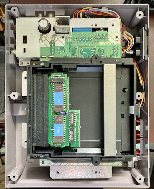 The top of the NES is open, exposing the bare cartridge PCB to logic probing. The two ROMs of the game are shown with blue sticky labels reading "PRG" and "CHR." There is a black wire running from a stuck out pin 22 on the PRG ROM to the underside of the board - on the wrong side, as it's going to capacitor positive instead of negative.