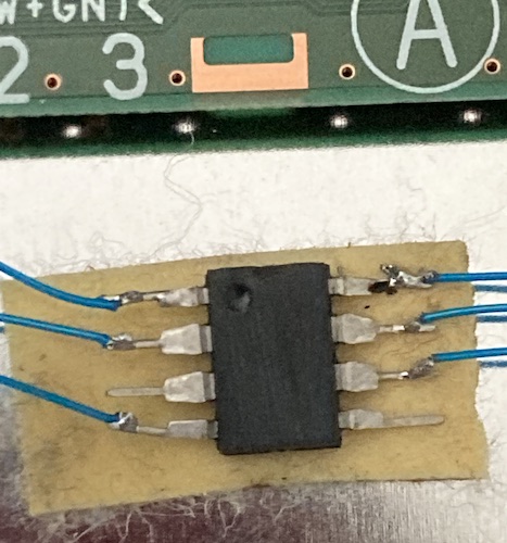 An 8-pin DIP with the top ground off is splayed onto some masking tape. Loose solder joints with lots of burned flux are present on the pins.