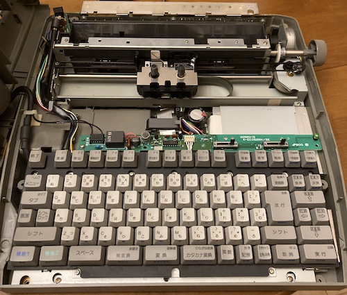 The top part of the case, including the display, has been removed and set on its side. The keyboard frame and printer are exposed.