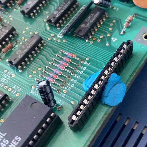 The new keyboard connector is held onto the board with blue sticky tack, so that it won't fall out when the board is flipped over to solder it in. In the background you can see an SN76489 sound chip. In the foreground, a TMS9918 video controller, and a 74LS138 multiplexer.