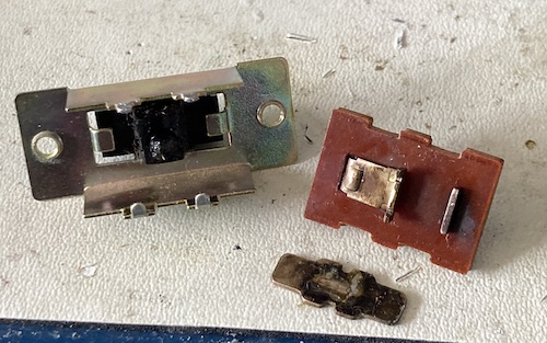 The parts of the power switch. From left to right: case, plastic toggle with rubber follower/spring, switching leaf, terminal plate. I'm not sure these are the names that the actual engineers of this switch would have used. For one thing, they'd be speaking Japanese.