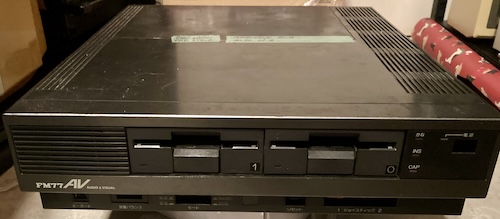 The FM77AV2, after having its power button damaged, sitting on a display plinth (an old power supply) in my storage pile.