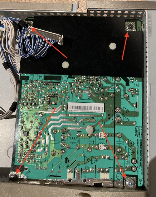 Red arrows point to the four screws that need to be removed to get the power supply out. Notice that one of the screws is denoted as the primary-side ground, and is a different kind of screw for some reason.