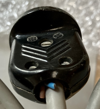 The Egyptian(?) power plug, with a brown and blue wire sticking out of it. It has a stamped callout reading what appears to be "DDR" and is held together by screws