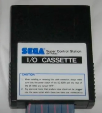 The "I/O Cassette" cartridge, with ribbon cable, which connects the SC-3000's expansion bus to the SF-7000. Courtesy of Joystick Division.