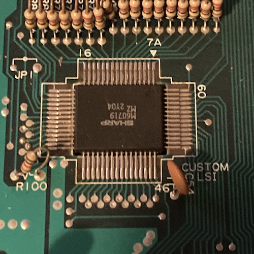 A QFP marked "Custom LSI" on the motherboard is pictured. Its label is Sharp M60719 MZ 2Y04, and it appears to have 60 pins, with 16 pins on each long side and 14 pins on each short side. A silkscreen mark is pointing to pin 1 with the legend "7A."