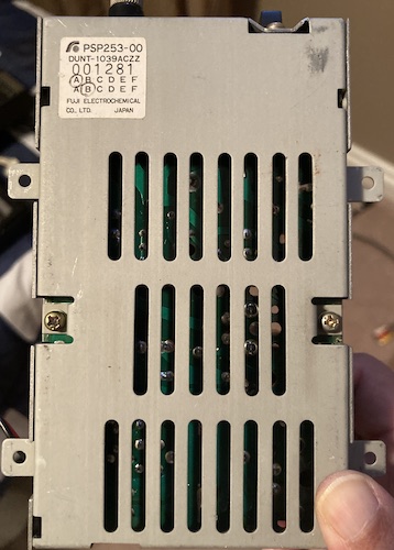 A steel box with some vents cut in it and a single-sided PCB inside. It is labelled PSP253-00 DUNT-1309ACZZ with Fuji Electrochemical makers' mark.